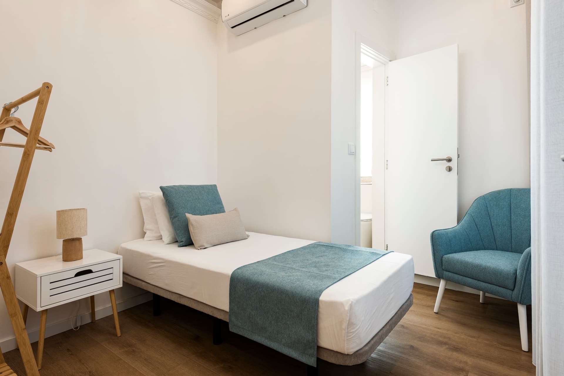 Suite individual do Madalena, com cama de solteiro, poltrona azul e WC en-suite